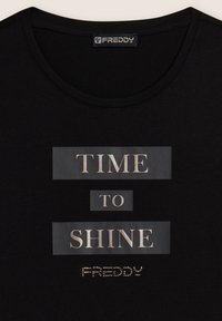 Camiseta negra con cuello redondo que presenta el texto plateado "TIME TO SHINE" y un pequeño logotipo con tachuelas "FREDDY" debajo del texto.