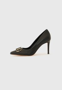 Svarte skinn høyhælte pump med spiss tå, med en gullfarget sirkulær spenne detalj på vampsiden og en smal stilett hæl.