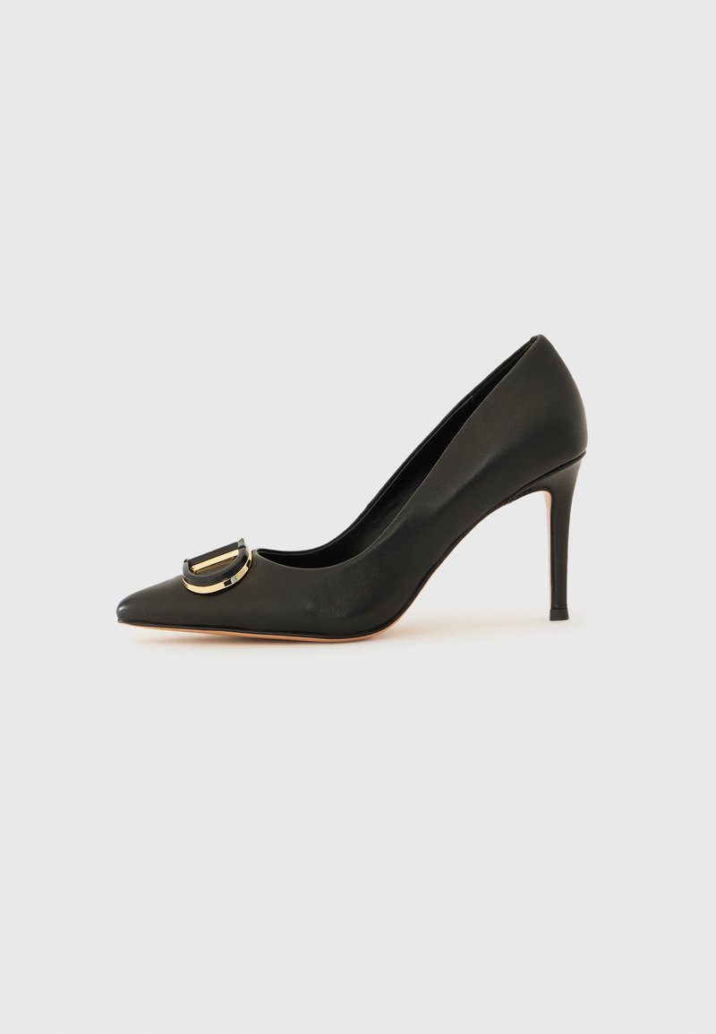 Svarte skinn høyhælte pump med spiss tå, med en gullfarget sirkulær spenne detalj på vampsiden og en smal stilett hæl.