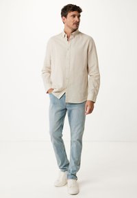 Chemise en lin beige à boutons avec un col, associée à un jean bleu clair et des baskets blanches. Texture lisse, design décontracté.