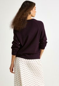 Paarse, gebreide trui met lange mouwen, geribde manchetten en halslijn. Gecombineerd met een off-white rok met stippen. Zachte textuur, casual ontwerp.