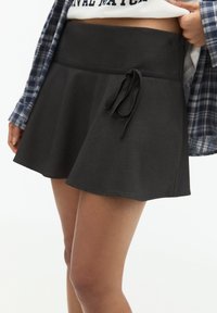 Jupe noire avec une large taille élastique dotée d'une fermeture à nouer. Le tissu semble doux et extensible, s'évasant doucement à partir de la taille.