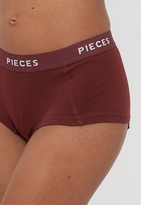 Bordowe bawełniane majtki hipster z miękkim paskiem, na którym widnieje napis "PIECES" w białym kolorze. Charakteryzują się gładką fakturą i przeszywanymi akcentami.