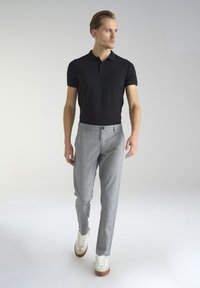 Czarna koszulka polo, szare spodnie w kratę, białe sneakersy z brązowymi podeszwami. Slim fit, krótkie rękawy, detal z guzikami na spodniach. Neutralne tło.