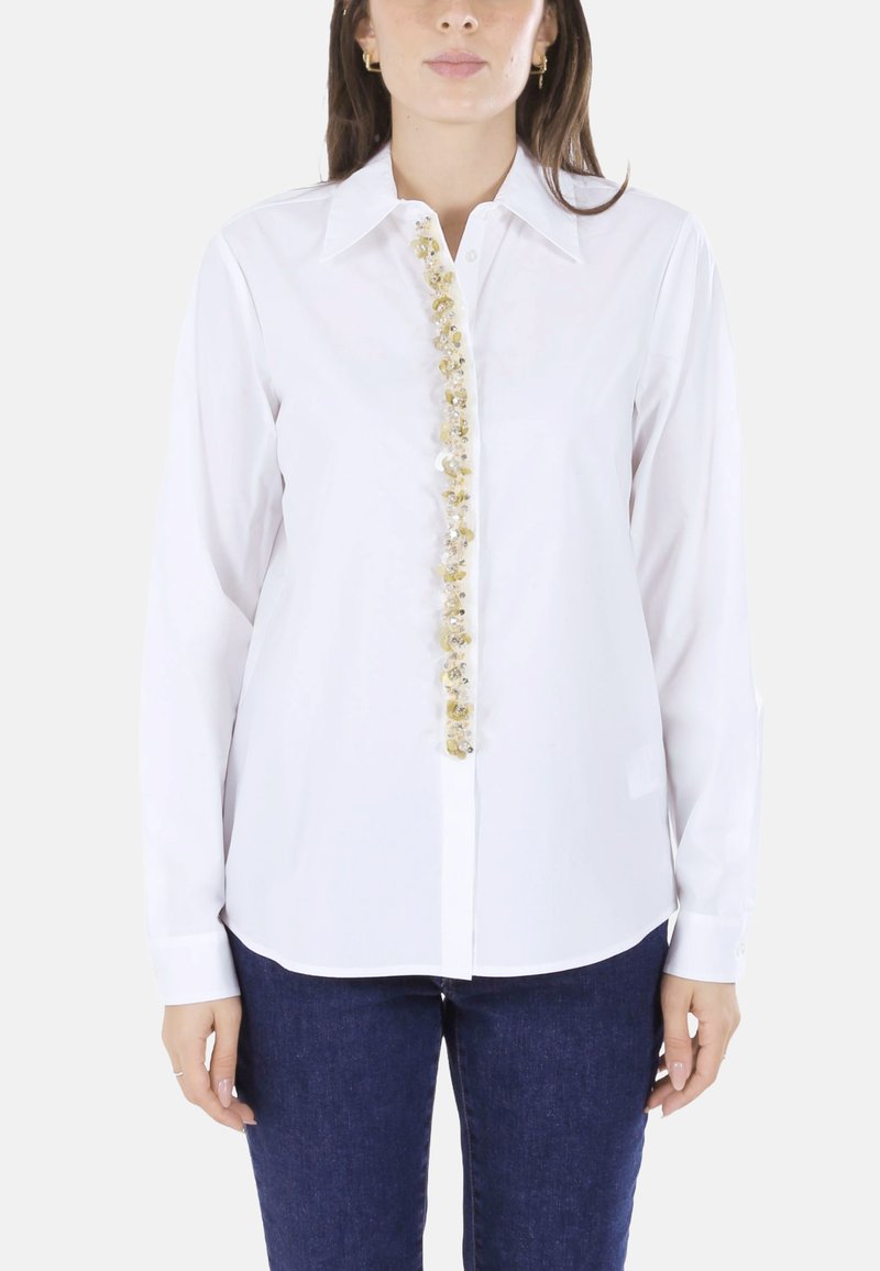Camicia bianca con bottoni e maniche lunghe, caratterizzata da una fila decorativa di strass dorati e trasparenti sul davanti.
