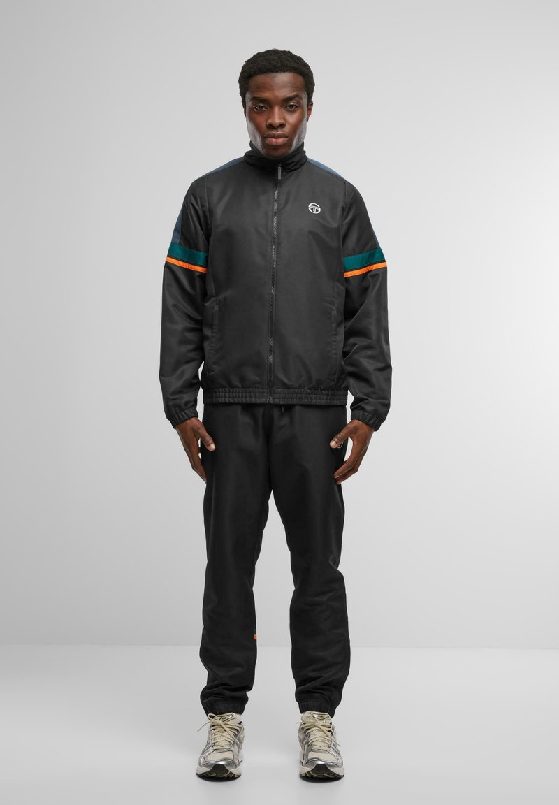 Chándal atlético negro con franjas en contraste de verde azulado y naranja, chaqueta con cremallera, puños elásticos y cinturilla elástica, combinado con pantalones a juego.