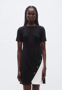 Vestido de manga curta em preto e branco, apresentando um design dividido diagonalmente com grandes botões prateados do lado preto. Textura suave.