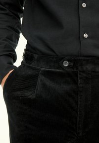 Zwarte corduroy broek met geribde textuur, voorzien van zijzakken en een knoopsluiting in de taille, gecombineerd met een zwart overhemdd. 