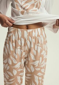 Biała bluzka z długim rękawem w brązowy nadruk liści; beżowe spodnie z białym wzorem liści; elastyczny pas; miękka, lekkka bawełniana tkanina.