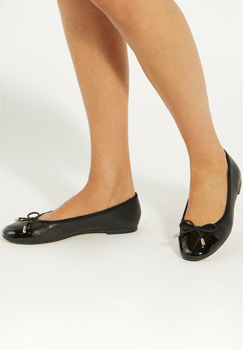 Black ballet flats featuring a glossy toe cap, soft leather upper, rounded shape, and a decorative bow with gold-tone accents.