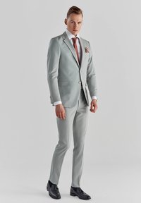 Jasnoszary garnitur o slim fit, biała koszula, krawat w wzory oraz strukturalna poszetka. Czarne buty dopełniają całość.