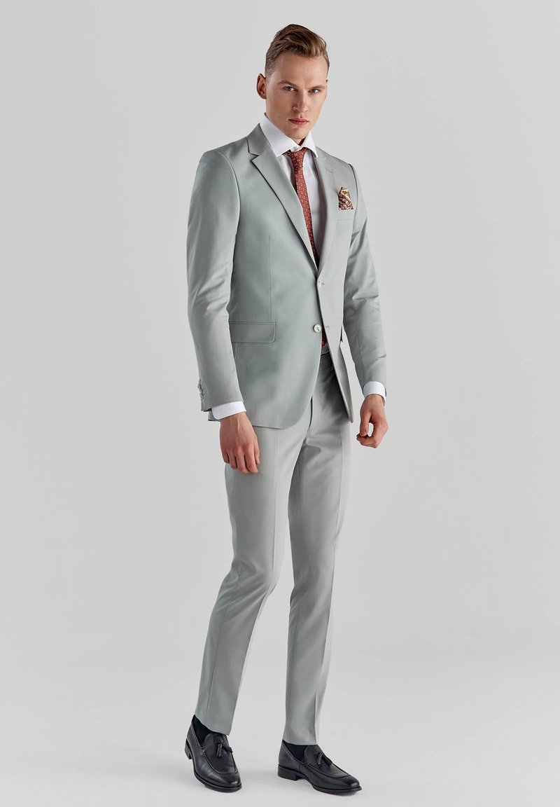 Jasnoszary garnitur o slim fit, biała koszula, krawat w wzory oraz strukturalna poszetka. Czarne buty dopełniają całość.