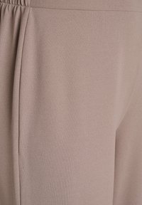 Mehka bež tkanina z gladko teksturo, z rahlim krojem in elastičnim pasom. Nežen nagubanje dodaja lahkotno, tekočo podobo.