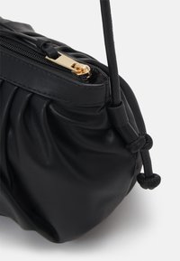 Borsa a mano in pelle nera con texture arricciata, dettagli in zip dorato e accenti a cordoncino annodato. Design compatto e morbido.