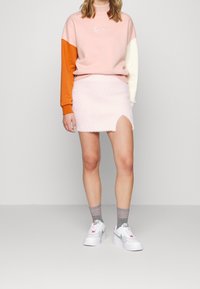 Felpa rosa chiaro con maniche arancioni e crema, abbinata a una mini gonna fuzzy rosa con uno spacco laterale. Sneakers bianche con dettagli verdi.