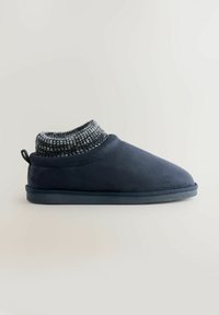 Navy modré semišové bačkory s pleteným, strukturovaným manžetou a kulatou špičkou. Design na nazouvání má odolnou, plochou gumovou podešev.