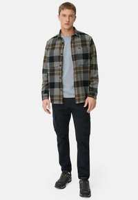 Rutig flannel skjorte i brun, grå og sort, båret over en lysegrå t-shirt. Sorte cargo-bukser og grå vandresko fuldender outfittet.