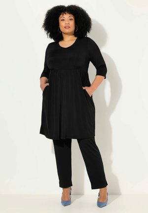 Robe noire à manches trois quarts avec taille froncée, poches, portée avec un pantalon noir et des talons bleus. Tissu lisse avec une coupe décontractée.