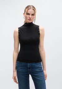 Μαύρο αμάνικο τοπ με λαιμόκοψη ζιβάγκο και τρουκς στους ώμους, κατασκευασμένο από λεία, ελαστική ύλη. Συνδυάζεται με μπλε τζιν παντελόνι.