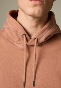 Hooded sweatshirt in dusty rose color, made of soft fabric. Features a drawstring with metal aglets and a smooth texture. Simple design.