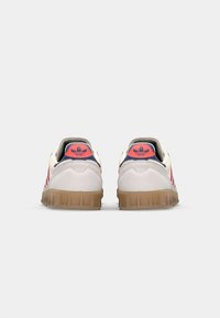 Biele tenisky s ružovými akcentmi, gumovou podrážkou a tromi červenými pruhmi. Štruktúrované očko na päte a polstrovaný golier. Retro dizajn s gumovou podrážkou.