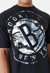 T-shirt noir avec un grand motif circulaire comportant "BROOKLYN" en haut et "NEW YORK" en bas, agrémenté de détails bleus et blancs.