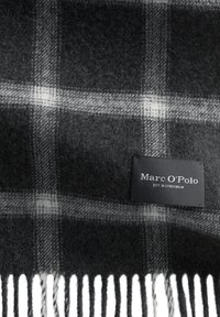 Szary wełniany szalik z czarno-białym wzorem w kratę, z frędzlami na brzegach oraz czarną metką z białym napisem "Marc O'Polo EST. W Sztokholmie."