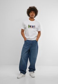 Hvid bomulds-t-shirt med et grafisk print af et farverigt dyrehoved. Sammen med løse blå denim jeans og hvide sneakers.