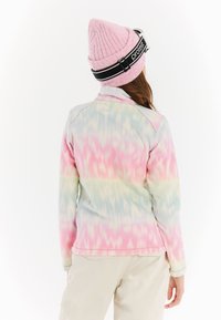 Fleeceová bunda v pastelových barvách s abstraktními vzory. Má vysoký límec a dlouhé rukávy, doplněná růžovou žebrovanou čepicí.