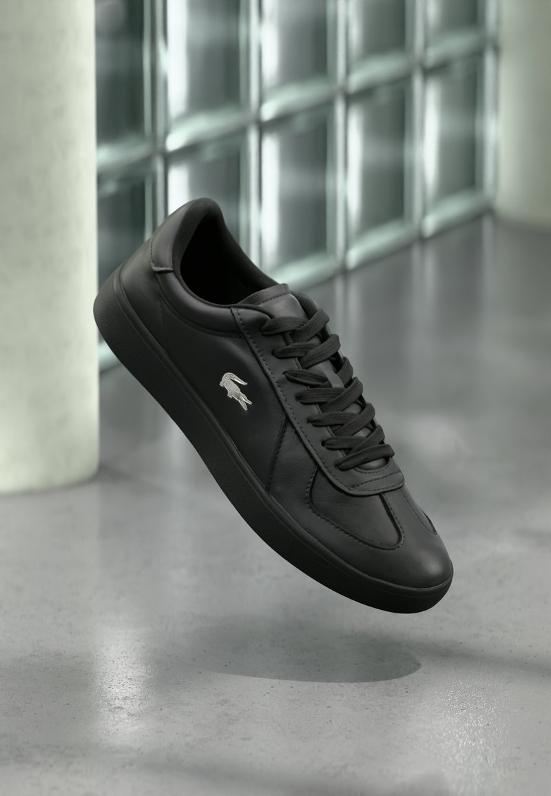 Black leather sneaker with a smooth texture, featuring a classic design, flat laces, and a small silver logo accent on the side.