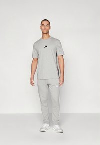 Pánský sportovní komplet obsahující lehké šedé tričko a odpovídající tepláky. Obě části mají volný střih a černé detaily.