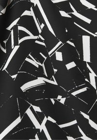 Schwarzer Stoff mit einem weißen abstrakten Muster, das scharfe, eckige Formen und Linien zeigt und eine dynamische visuelle Textur schafft.