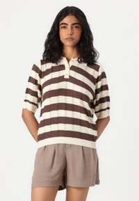 Haut en tricot à manches courtes rayé crème et marron avec un col et trois boutons. Motif texturé avec un ourlet côtelé, associé à un short marron.