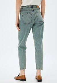 Ljust blå höga jeans med avslappnad passform, försedda med två bakfickor och fransdetalj i fållarna. Kompletterat med bruna slip-on-skor.