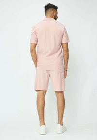 Chemise rose clair à col avec des manches courtes, assortie à un short. Le tissu présente de légères rayures verticales. Des baskets blanches complètent le look.