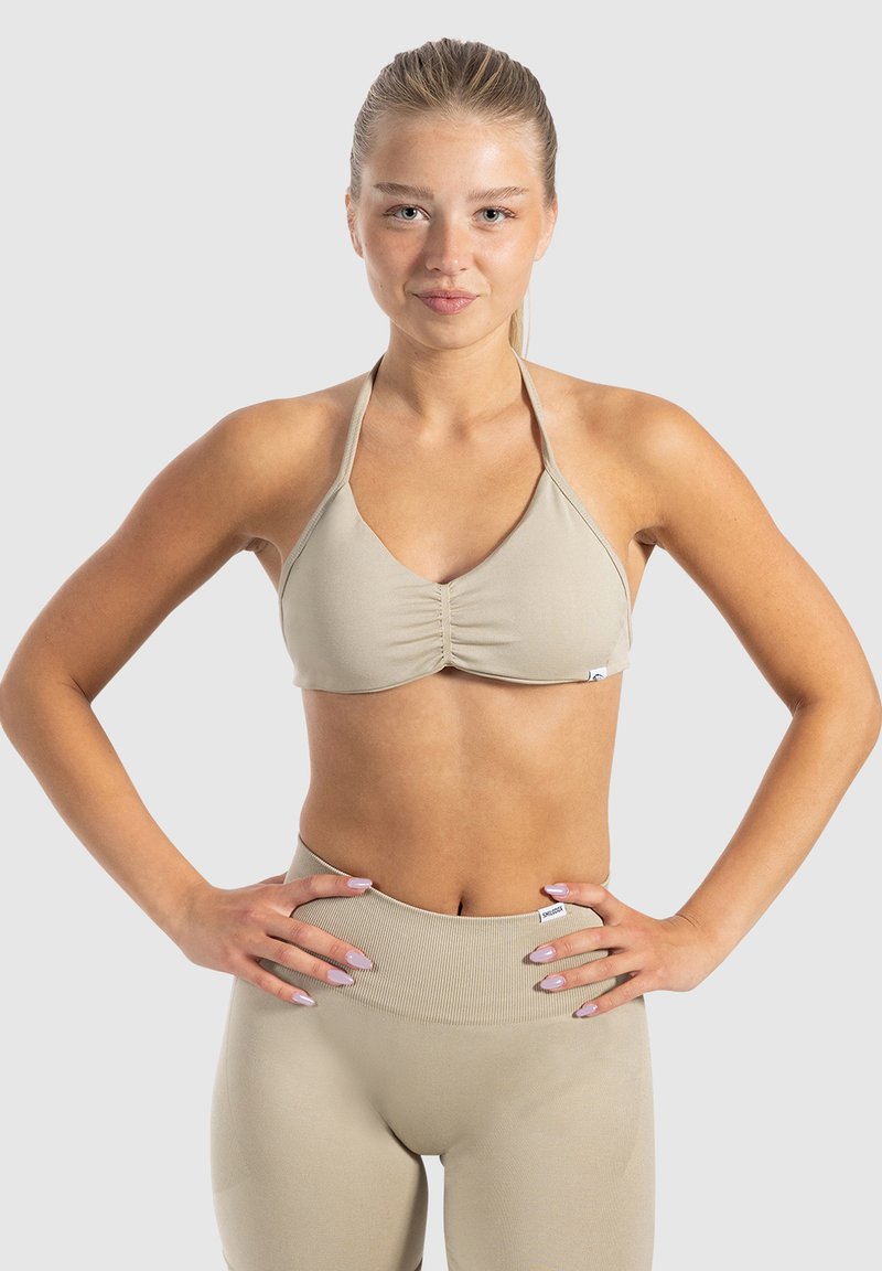 Top de bikini beige style halter avec des détails froncés, associé à un legging taille haute assorti. Tissu lisse et extensible avec peu de quincaillerie.