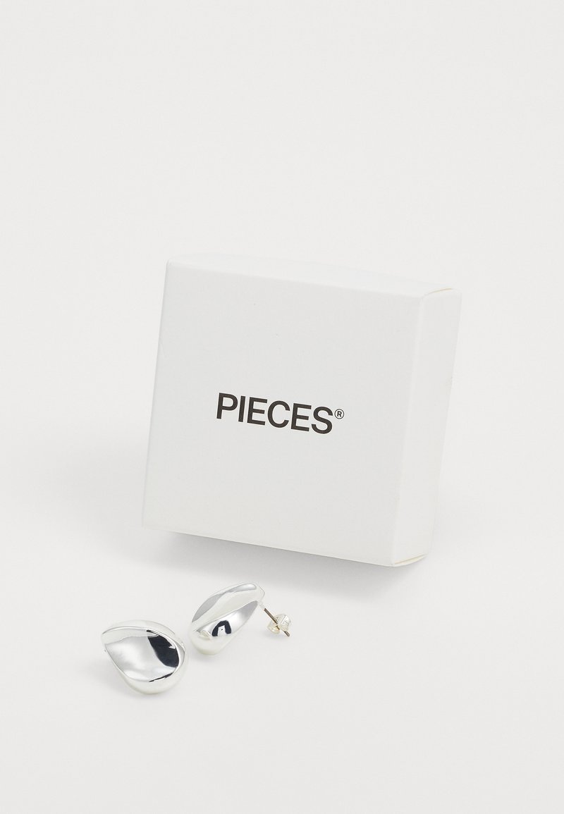 Boucles d'oreilles en métal argenté en forme organique, avec une finition brillante. Accompagnées d'une boîte blanche étiquetée "PIECES."