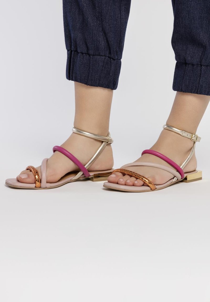 Sandales plates multicolores avec des brides roses et dorées, une semelle neutre et des accents métalliques au niveau du talon. Texture en cuir lisse.