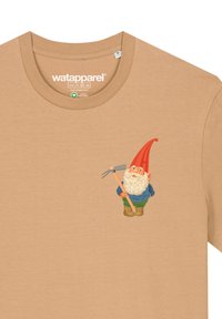 Beige katoenen T-shirt met een grafisch ontwerp van een gnoom met een rode hoed, blauwe shirt en groene broek, die een hark vasthoudt.