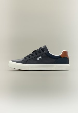 Alacsony szárú fekete sportcipő fehér talppal, fekete fűzőkkel, barna sarokdísszel és "Lee" logóval az oldalon.