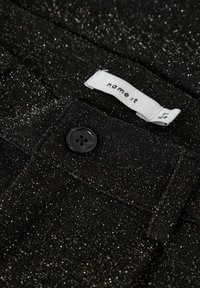 Črne hlače z teksturirano bleščico, z črnim gumbom za zapiranje in belim etiketom z napisom "name it" na pasu.