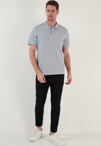 Světle modrá polo tričko s texturovanou tkaninou, krátkým rukávem a knoflíkovou légou, kombinované s černými slim-fit kalhotami a bílými teniskami.