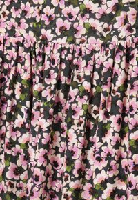 Blumener Stoff mit schwarzem Hintergrund, der kleine pinke Blumen und grüne Blätter zeigt, mit strukturierten Falten für zusätzliche Details.