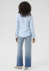 Light blue long-sleeve shirt with white paisley pattern, paired with faded blue wide-leg jeans and beige flats.