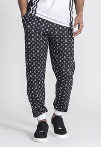 Zwarte joggerpants met witte logo's en patronen, elastische manchetten en een relaxed fit, gekoppeld aan zwarte sneakers.