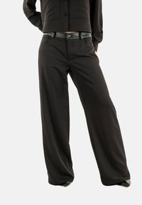 Pantaloni neri a gamba larga realizzati in tessuto morbido, con vita alta, una cintura nera lucida e tasche laterali. Vestibilità su misura con una silhouette fluida.