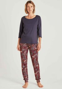Marineblauwe longsleeve top in combinatie met kastanjebruine broek met een bloemen- en dierenpatroon. De top heeft een ronde halslijn, de broek heeft elastische manchetten.