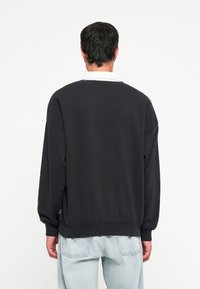 Svart sweatshirt med oversized passform, ribbede mansjetter og nederkant, myk tekstur, rund halslinning, brukt sammen med lyseblå denimjeans.