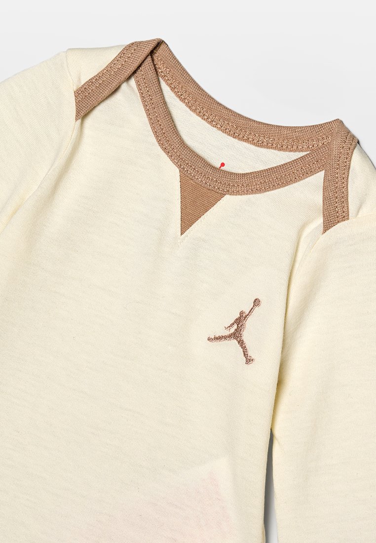 Camisa de manga larga color crema con cuello marrón y acentos en los hombros, con un logotipo de Jordan marrón bordado en el pecho.