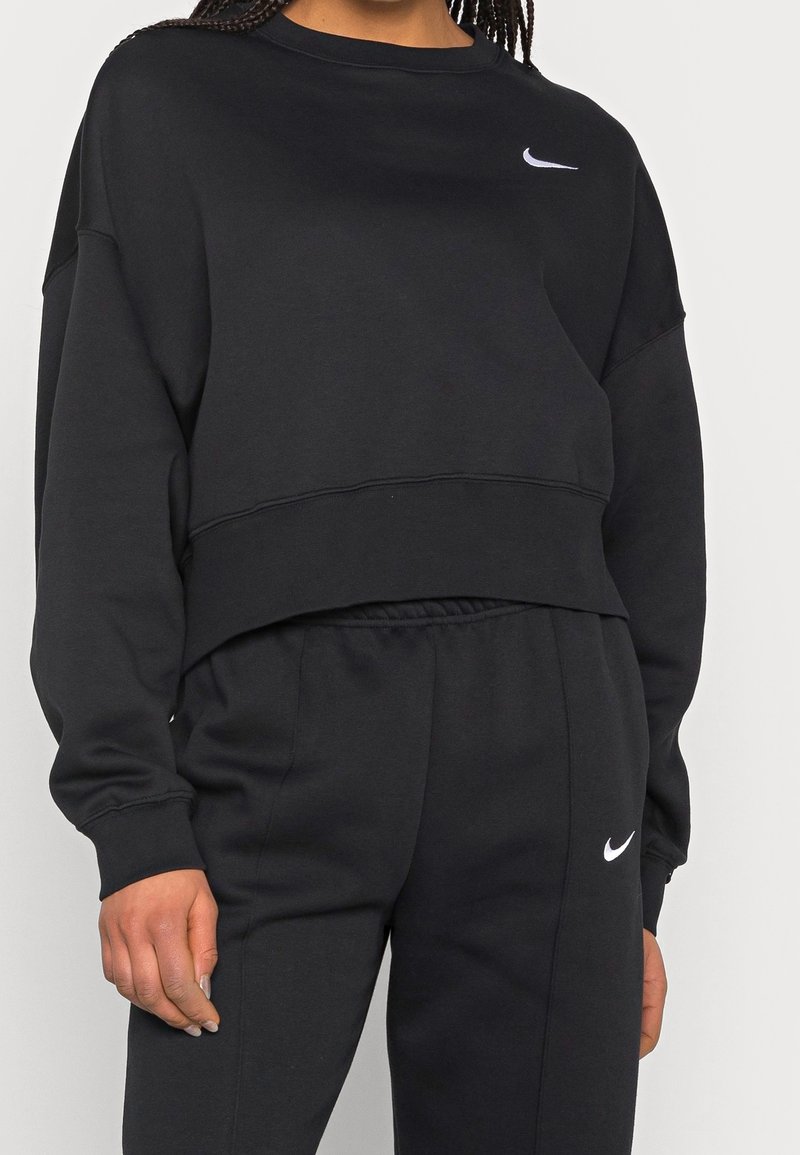 Black cropped sweatshirt with round neckline and long sleeves, featuring a white Nike logo on the chest. Made from soft fabric.